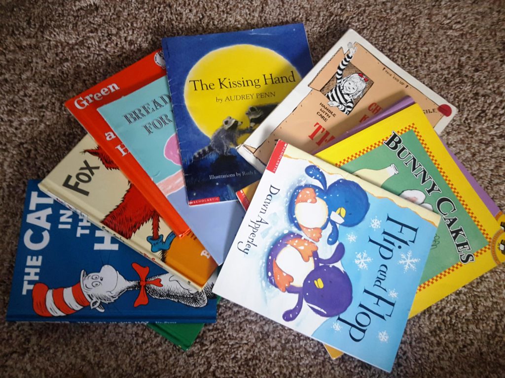 Colorful children's books are fanned out on a plush tan carpet, including the Cat in the Hat and The Kissing Hand